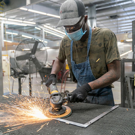 Apprenticetice wearing baseball cap and mask using a grinder on a piece of metal